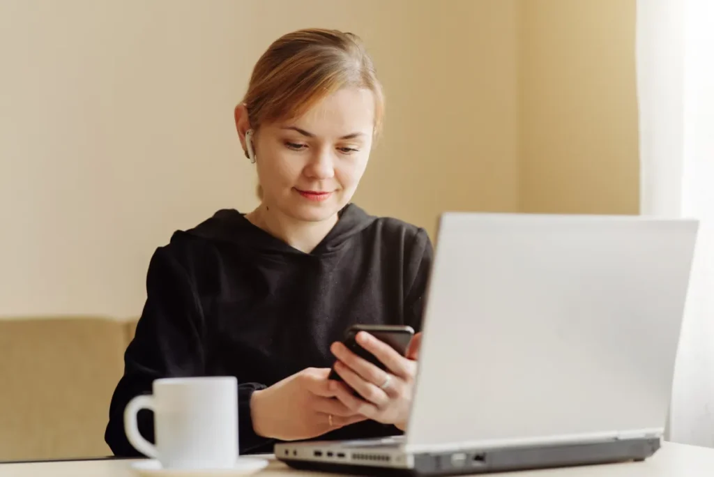 Kobieta korzysta z telefonu i laptopa przy biurku. Zdjęcie ilustracyjne.
