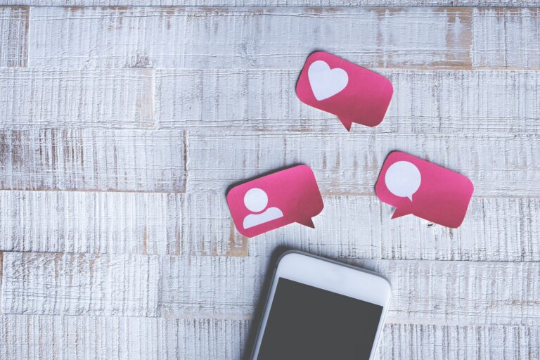 Telefon na drewnianej podłodze, nad nim popularne reakcje w social mediach.